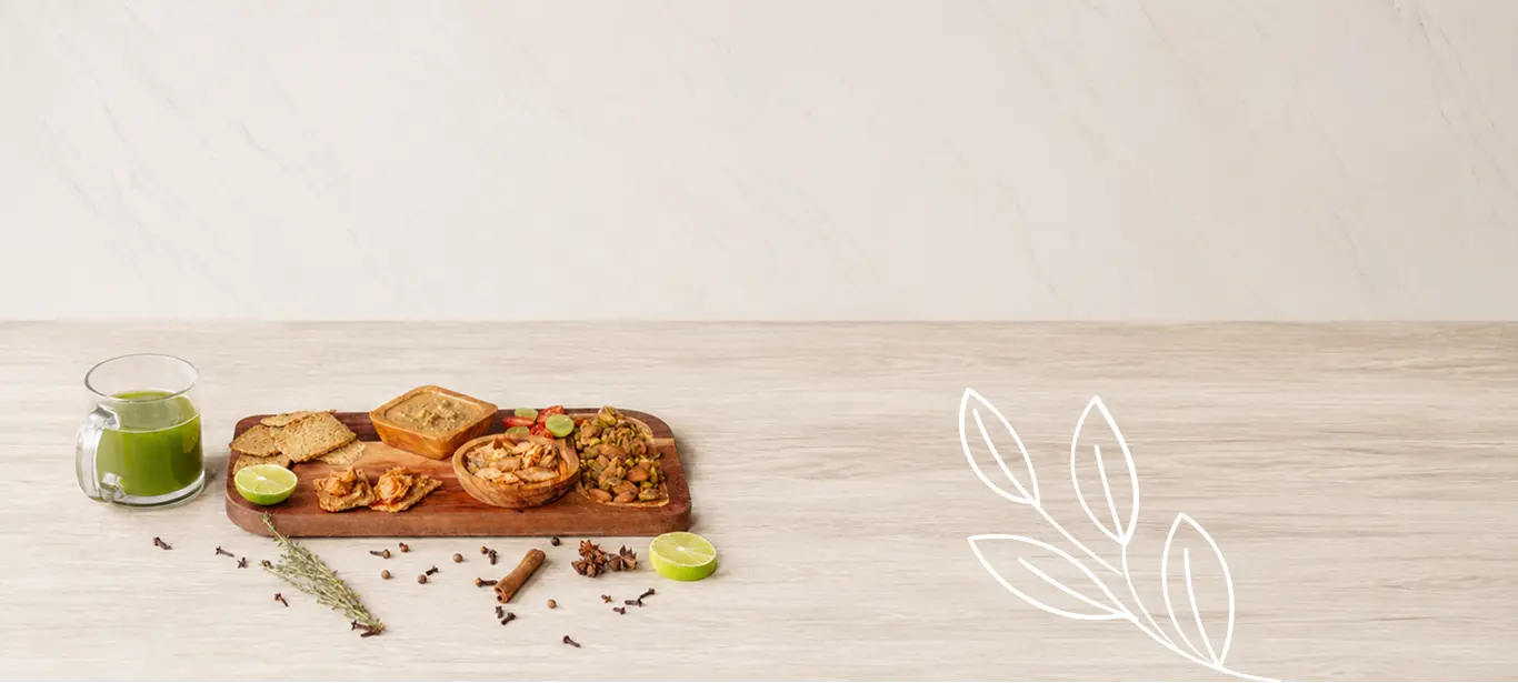 RaizBack gourmet snack spread with green juice, artisan crackers, savory dips, pistachios, lime, herbs, and spices on a wooden board.
