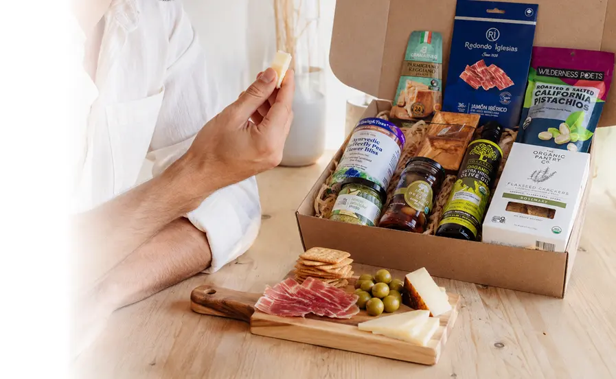 RaizBack curated gourmet gift box with Jamón Ibérico, Parmigiano Reggiano, pistachios, olive oil, crackers, olives, and artisan specialty foods.